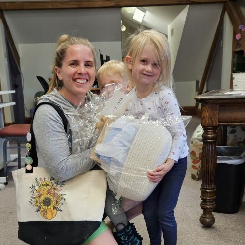 A smiling woman and kids hold a gift basket of prizes from the library Summer Experience.