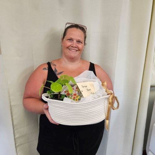 A smiling woman holds a gift basket of prizes from the library Summer Experience.